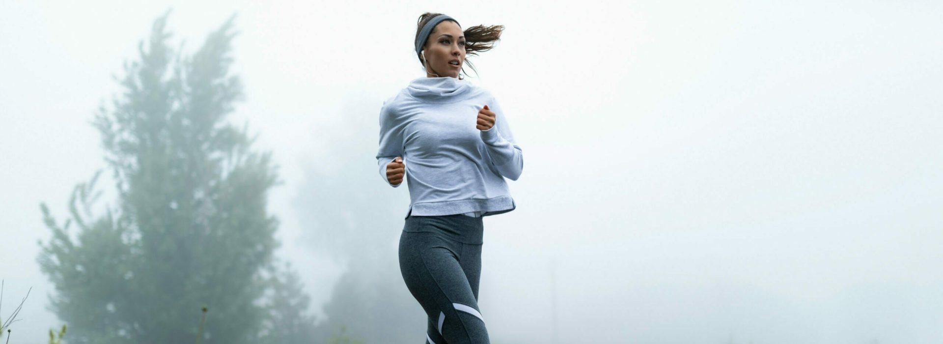 Determined female runner jogging through misty filed in the morning. Copy space.